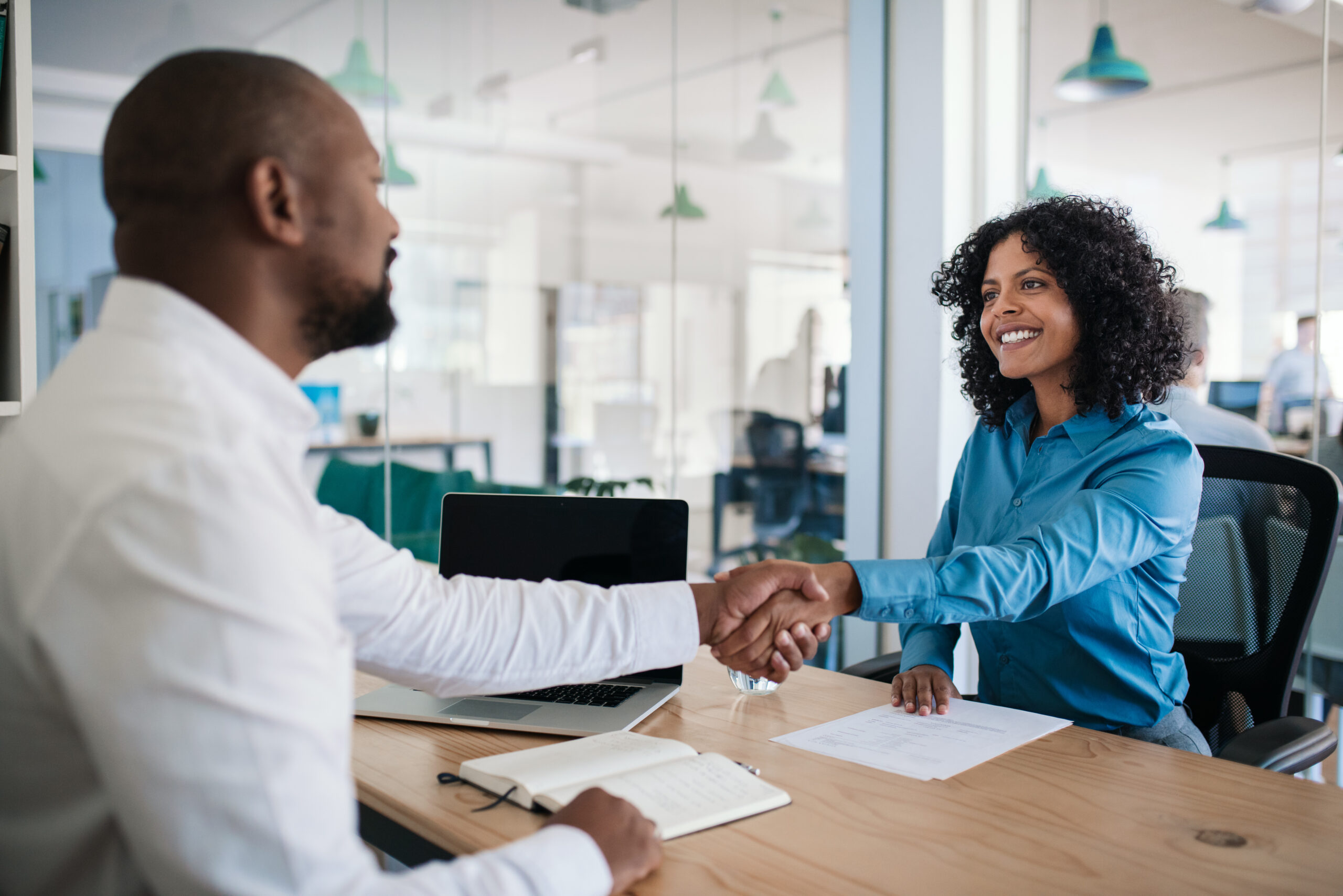 manager sitting at his desk in an office shaking hands with a job applicant after an interview