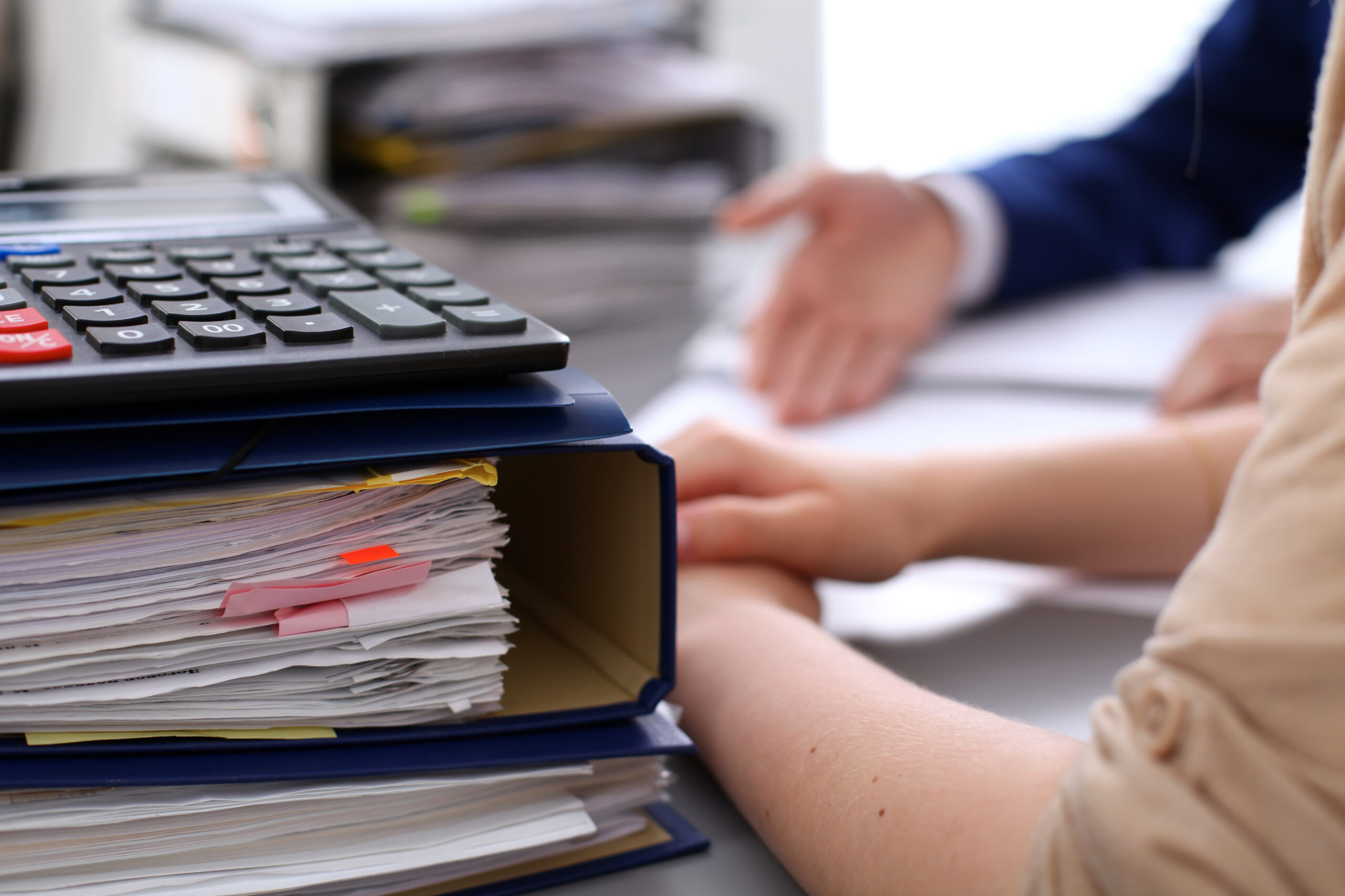 Binders with papers are waiting to be processed with businessman and secretary back in blur