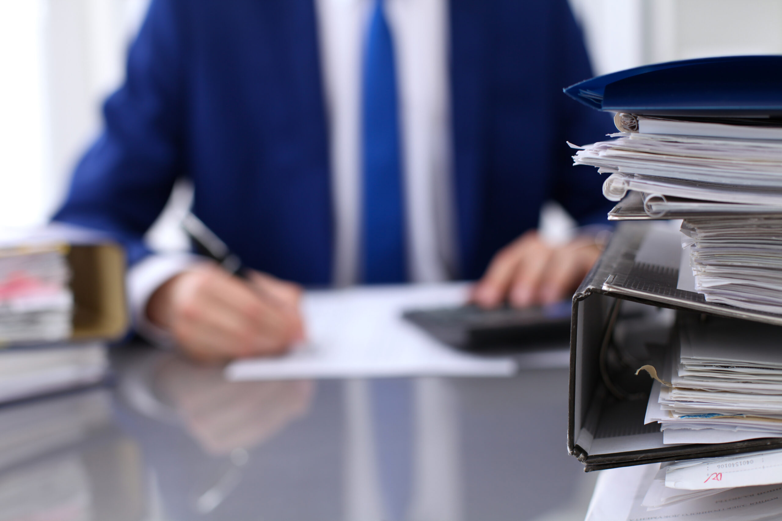Binders with papers are waiting to be processed with businessman back in blur